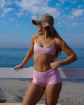 Woman in pink bikini and hat standing on a beach with ocean and sky in the background