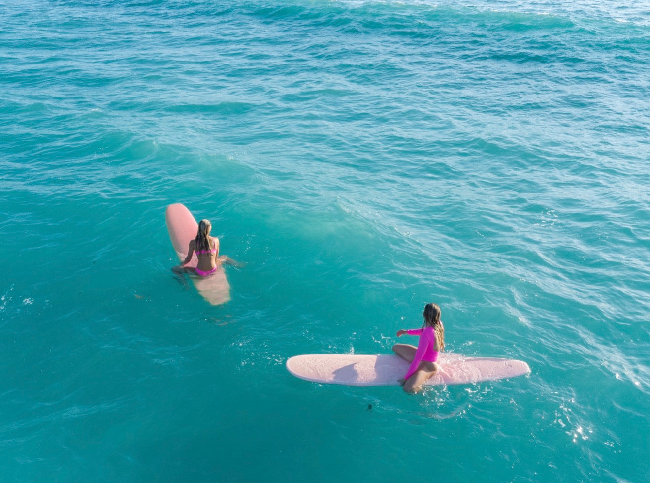 Two people on pink surfboards in the ocean.